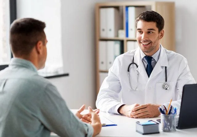 Doctor sitting behind a desk, smiling and talking to a male patient