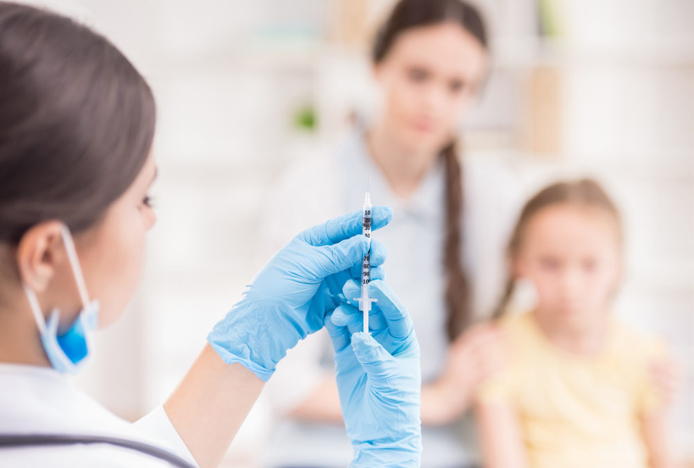 Doctor doing vaccine injection to blond little girl.