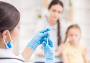 Doctor doing vaccine injection to blond little girl.